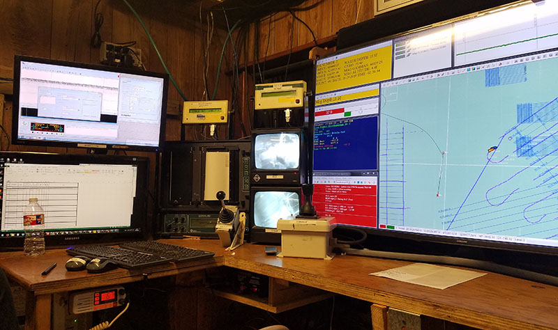 The primary survey station includes multiple computers logging various data sets; the vessel’s navigation track is visible at right.