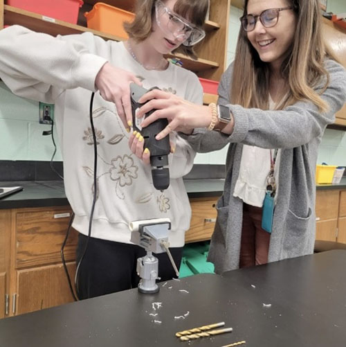 Teacher Emily McAfee (right) guides a student in drilling holes in PVC pipes used to construct a remotely operated vehicle.