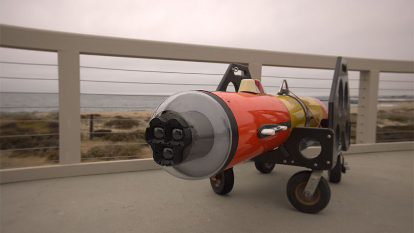 Autonomous underwater vehicle with an orange and yellow body on a concrete surface near the sea.