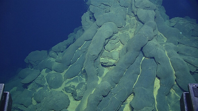 A mount of pillow lava. These pillow basalts form when basaltic lava erupts underwater. Cold seawater chills the erupting lava, creating a rounded tube of basalt crust that looks like a pillow. As the newly erupting lava pushes through the chilled basalt crust, it can form scratches on the pillow surface, called striations.