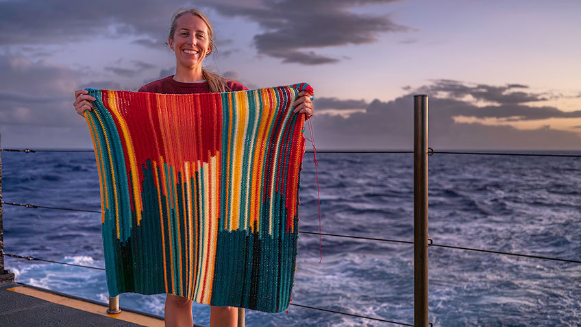 NOAA Ocean Exploration Internship Program Coordinator Jesse Gwinn on the fantail of NOAA Ship Okeanos Explorer with her in-progress bathymetry blanket, which illustrates ocean depth data collected during the Beyond the Blue: Johnston Atoll Mapping 2 expedition.