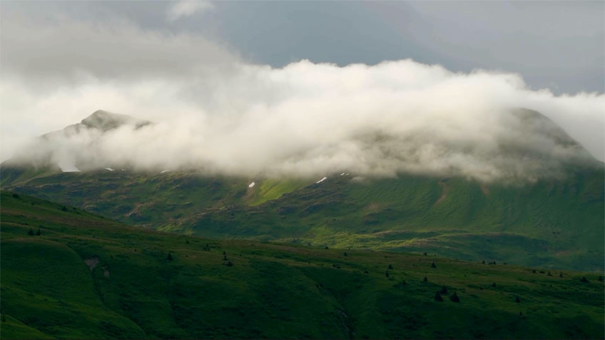 A landscape of green mountains partially covered by low, white clouds.